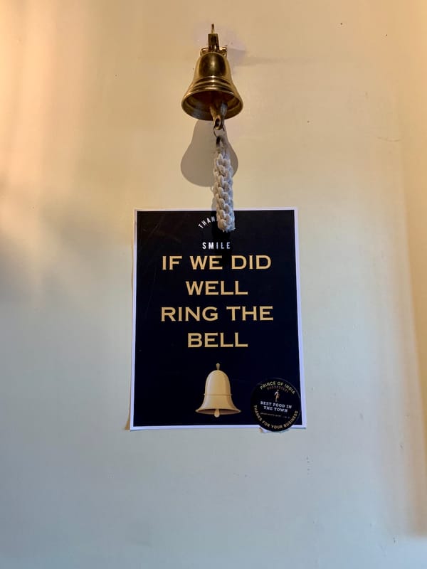 a poster on a wall saying 'Smile. If we did well, ring the bell,' with an image of a bell at the bottom