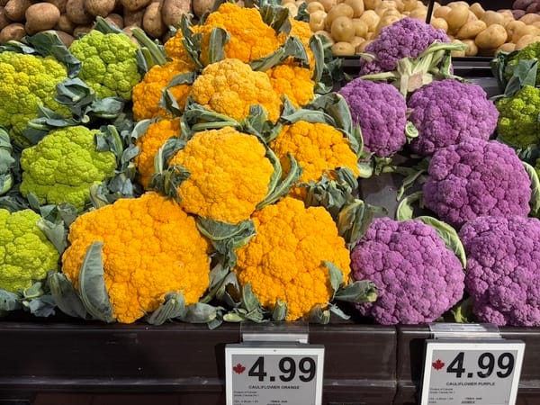 heaps of green, orange, and purple coloured cauliflowers on a shelf in a grocery store