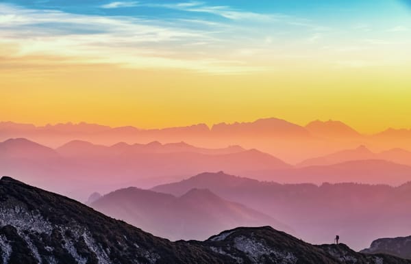 pink-toned silhouettes of mountain ranges and a solo hiker in the foreground