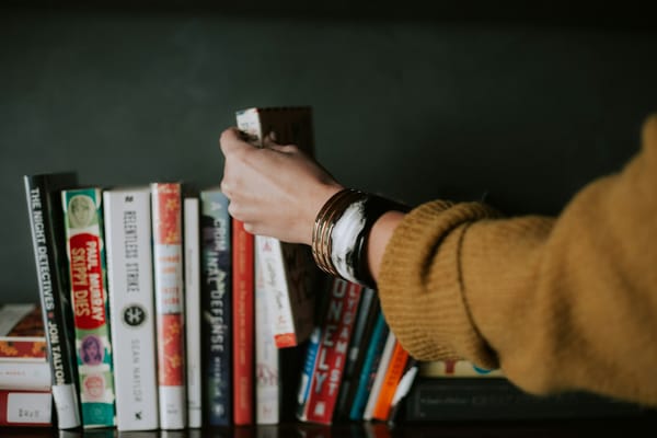 a woman's hand picking up a book from a stack of several on a shelf