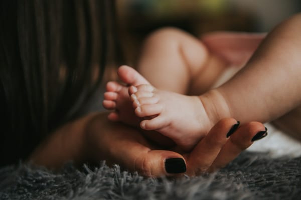 infant's feet held by a woman's hand resting on a grey blanket
