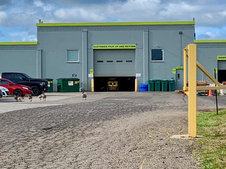 rear of a warehouse with an automated vehicle behind a shutter and a sign stating 'Customer pick up and return' above it