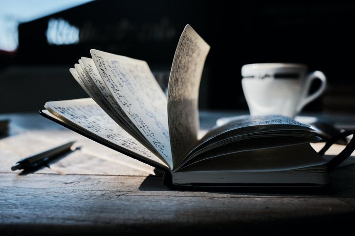 an open journal with pen and a cup of coffee on a wooden desk