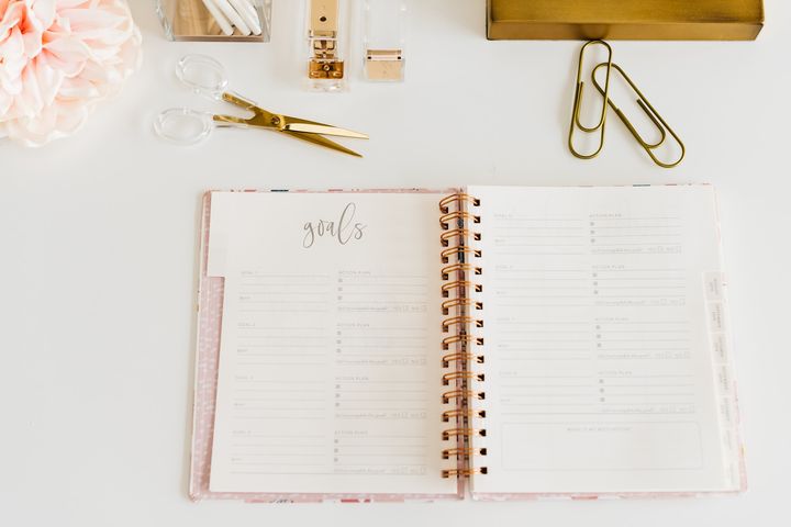 an open spiral planner set an a table besides a pair of gem clips, a pair of scissors, and a floral arrangement