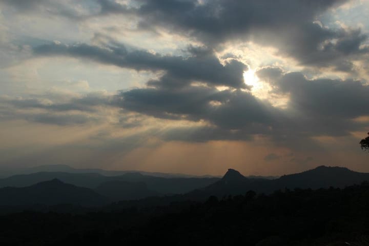 sun behind clouds in the sky above hilltops