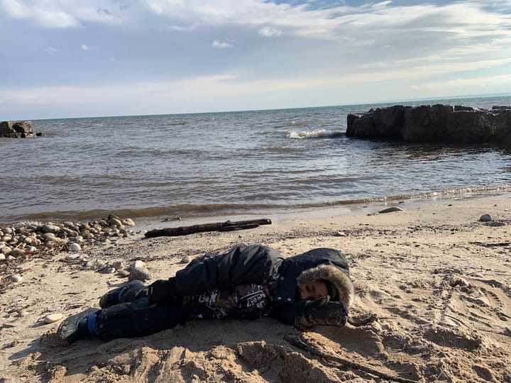 a child dressed in winter gear lying on a sandy beach