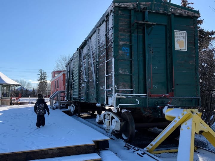 a red caboose coupled to a green freight car with a poster on it saying 'apple route'