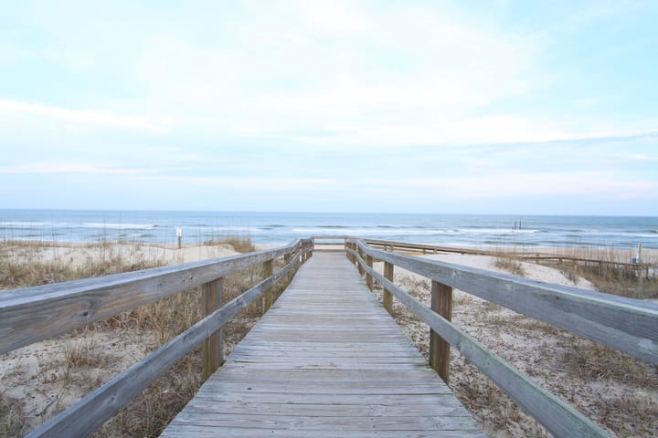 boardwalk leading to a sandy beach and the ocean beyond under a pale blue sky with white clouds