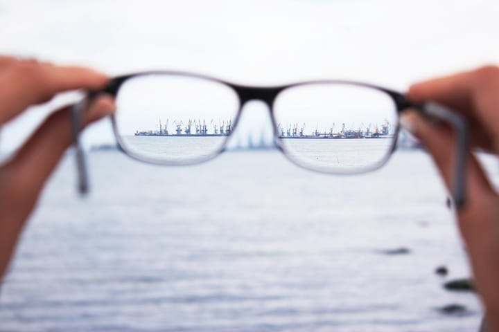 port cranes in the horizon coming into focus when viewed through spectacle lenses against a blurry backdrop of the ocean