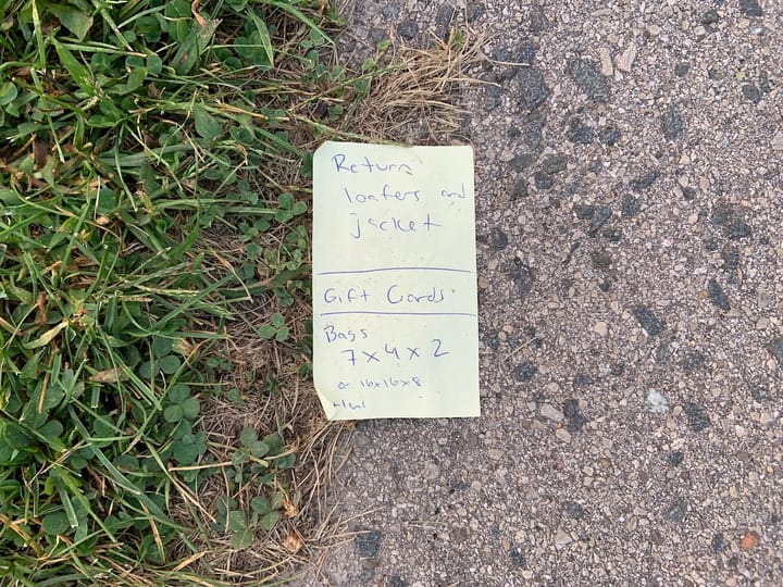 a shopping/to-do list on a yellow post-it note lying on the ground, partly on grass, partly on a concrete path