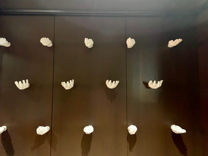 a wooden wall from which white, ceramic hands protrude in different gestures