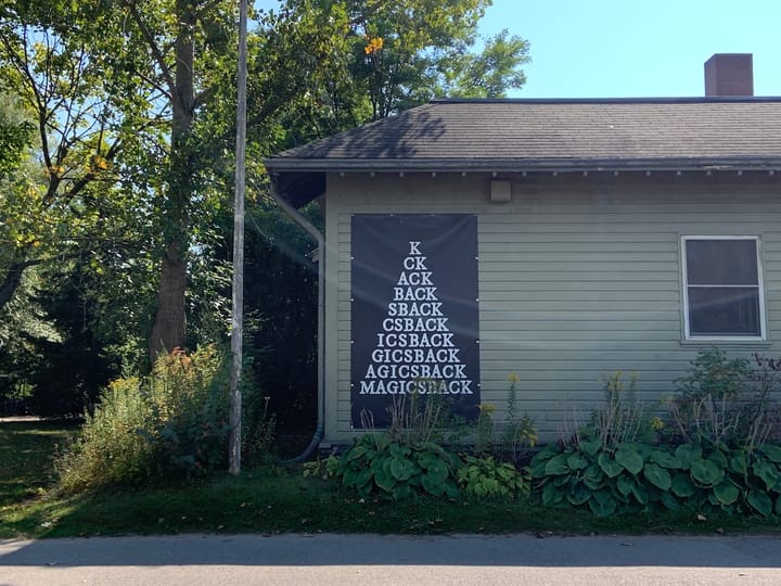 a one-storeyed house with a large black poster taped to its wall reading 'MAGICSBACK' adding one letter at a time