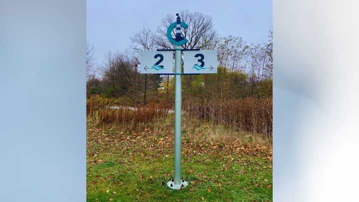 a pole with signs labeled 2 and 3 with arrows pointing left and right, respectively, with a large letter C and a lighthouse design on the top
