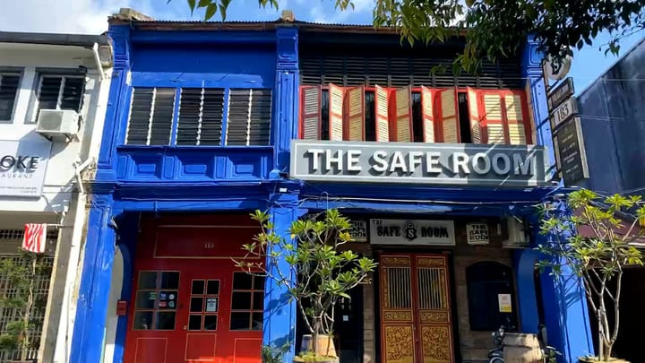 a blue, two-storied building with red doors and windows and a board saying 'The Safe Room'