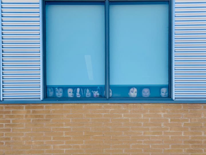 view of a window behind which sit a number of mannequin heads looking out