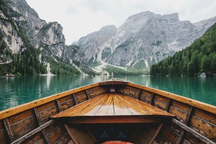 helm of a brown wooden boat moving towards a mountain range on a green lake