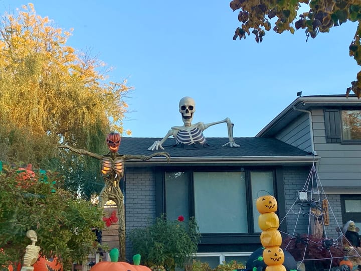 a skeleton rising from the rooftop of a split-level house decorate with Halloween decorations on the front lawn