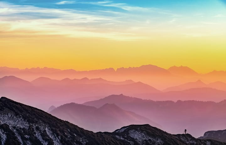 pink-toned silhouettes of mountain ranges and a solo hiker in the foreground