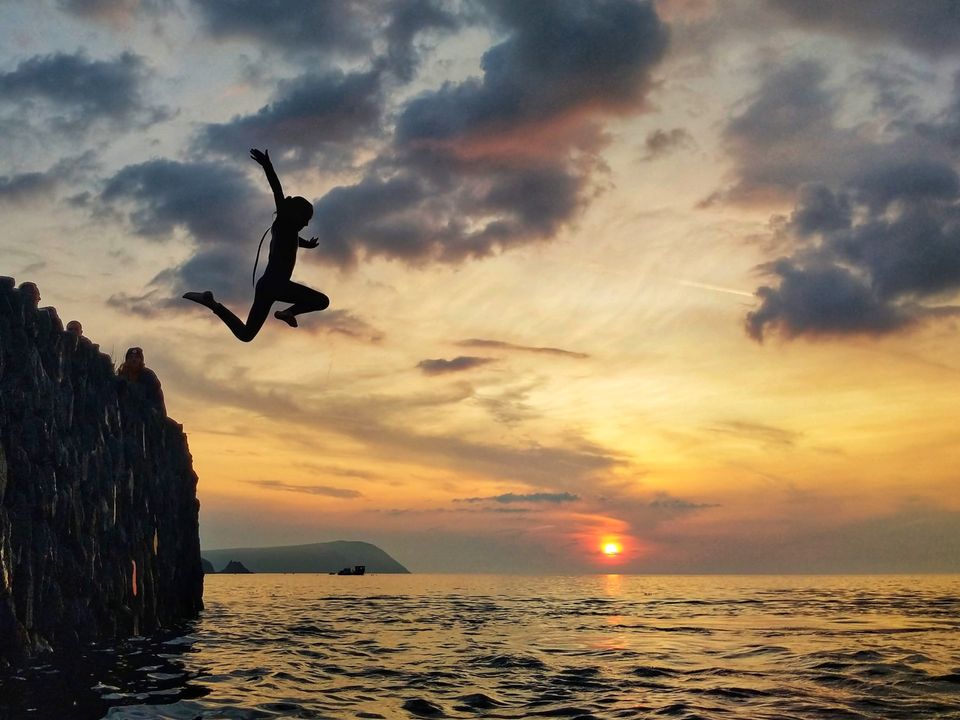 child diving off a cliff into the sea with the sun setting in the background 