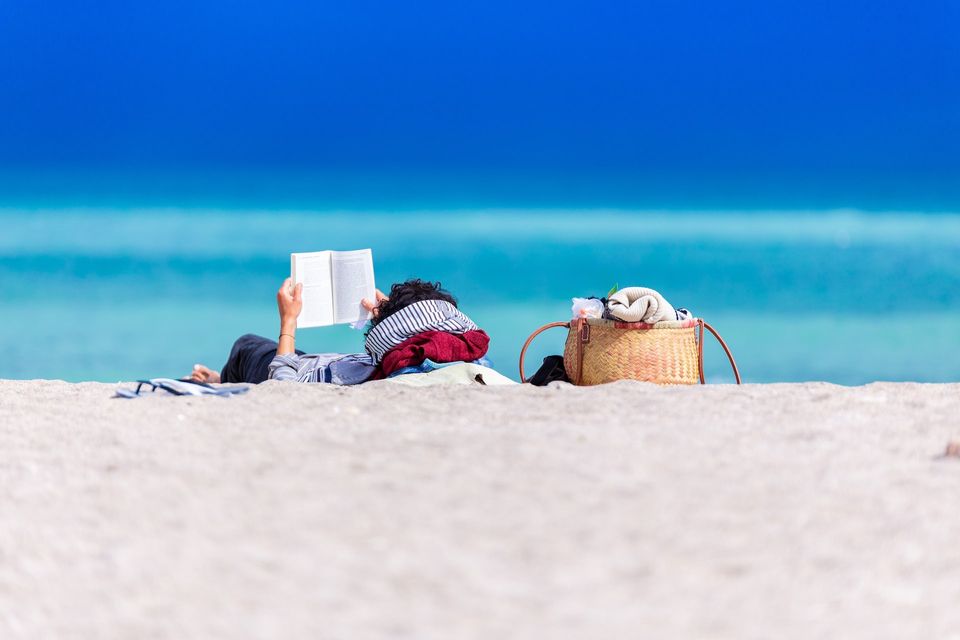 image of a person lying on a beach and reading a book
