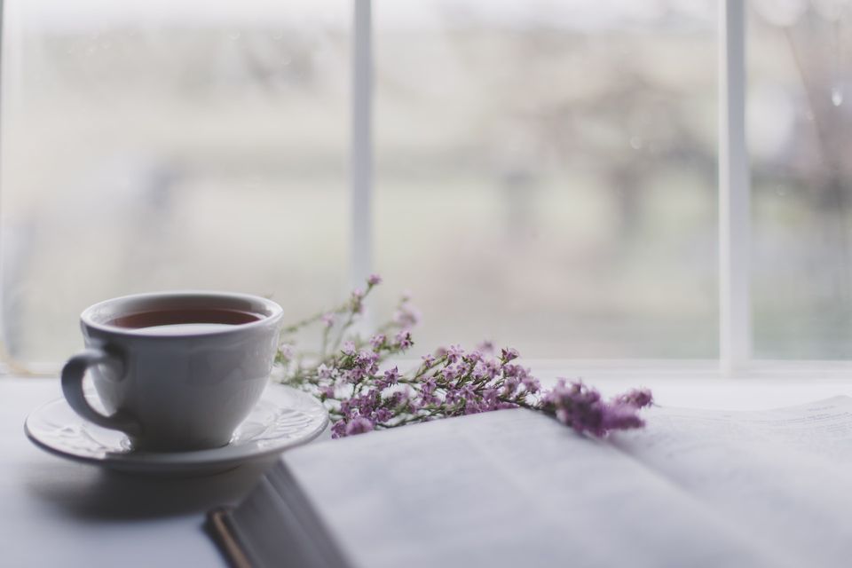 an open book, a sprig of lavender, and a cup of tea by a window-sill