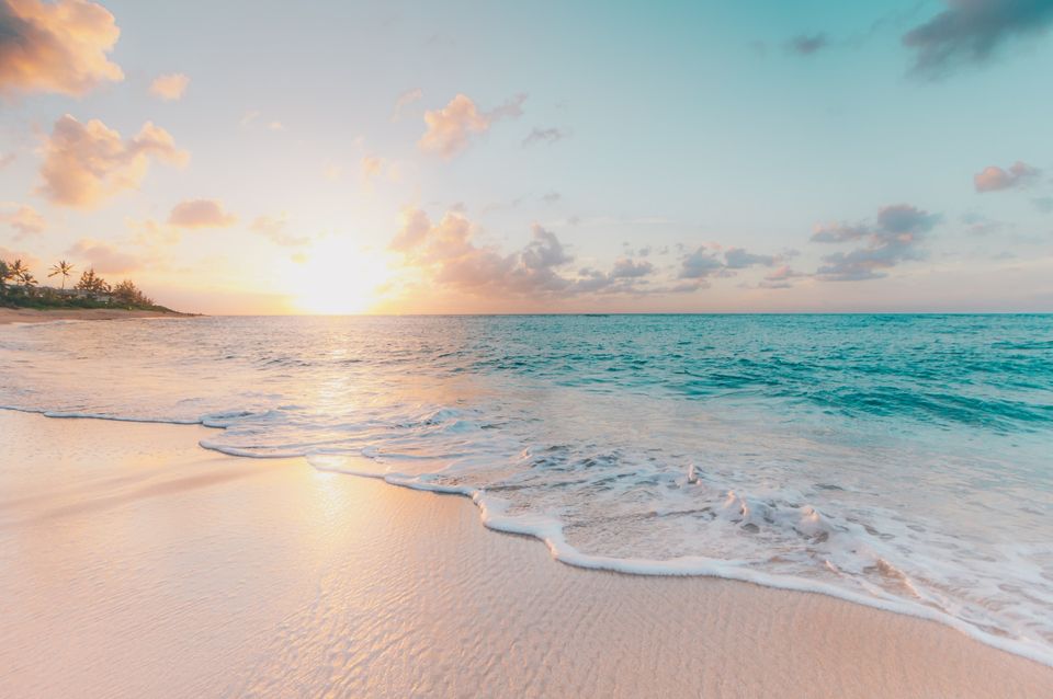 turquoise sea waters on a sandy beach with the sun in the horizon
