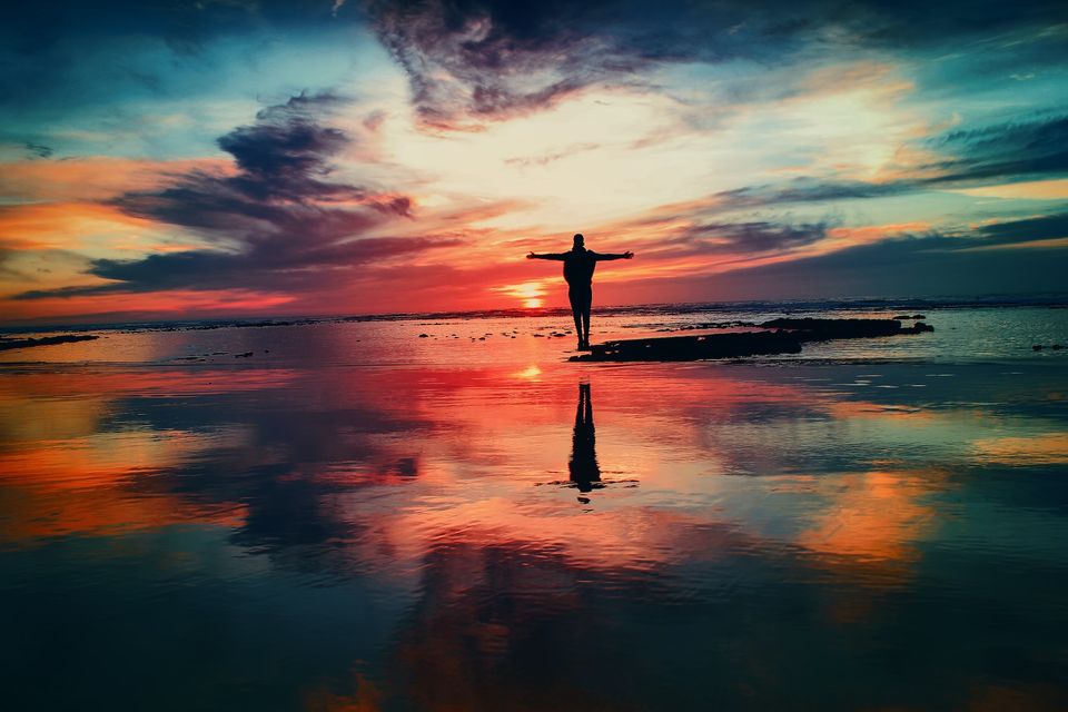 silhouette of a person with arms spread wide open and standing on a beach under a sunset sky