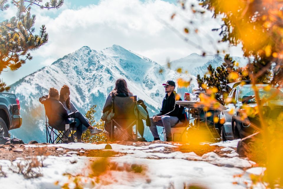 group of people sitting on foldable chairs in a circle overlooking snow-capped mountains
